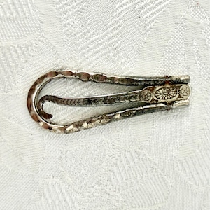 May include: A silver-toned money clip with a hammered texture on the edges. The clip features a decorative floral design on the clasp. The clip is designed to hold folded bills and is made of metal.