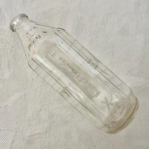 Pode incluir: Uma garrafa de vidro transparente com um gargalo estreito e uma base larga. A palavra PYREX está gravada em letras maiúsculas grandes ao longo da lateral da garrafa. Perto do gargalo, o texto diz REG. U.S. PAT. OFF. e MAX.