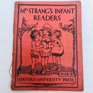 Puede incluir: Portada de libro vintage roja con el título "Mrs Strang's Infant Readers" en negro. La ilustración muestra a tres niños leyendo un libro, enmarcada por motivos florales y de pájaros negros. Publicado por Oxford University Press.