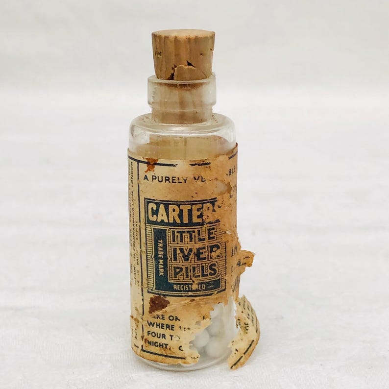 May include: A small glass bottle with a cork stopper filled with white pills. The label reads "Carter's Little Liver Pills, Trade Mark Registered".