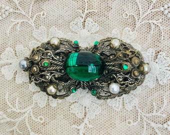 May include: A vintage brooch with a green glass cabochon surrounded by ornate silver filigree and faux pearls.
