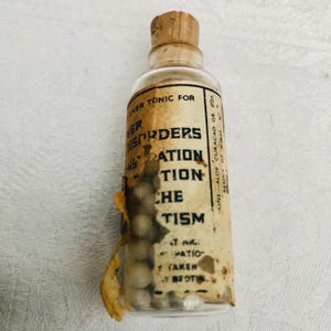 May include: A small glass bottle with a cork stopper filled with white pills. The label reads "Liver Tonic for Disorders of Digestion,  Aches,  Catarrh.  Contains Aloe Curacao Gr. 025. Resin Gr. 00625."