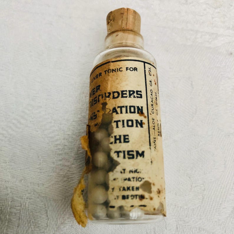 May include: A small glass bottle with a cork stopper filled with white pills. The label reads "Liver Tonic for Disorders of Digestion,  Aches,  Catarrh.  Contains Aloe Curacao Gr. 025. Resin Gr. 00625."