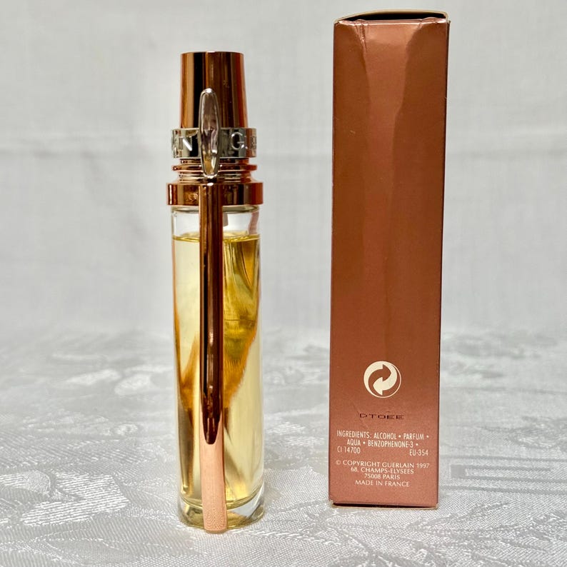 May include: A perfume bottle with a gold-colored cap and applicator, filled with a light yellow liquid. The bottle is next to a matching rectangular box. The box has text that includes "DTOE" and "MADE IN FRANCE".