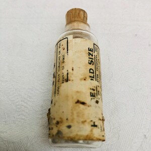 May include: A small, clear glass bottle with a cork stopper and a label that reads "ELD SIZE" and "AFTER PRODUCTS INC".