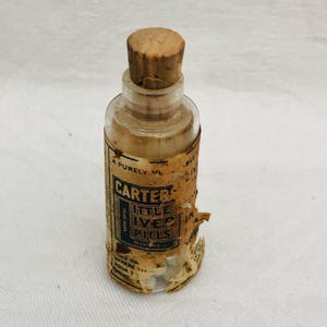 May include: A small glass bottle with a cork stopper. The bottle is labeled "Carter's Little Liver Pills" and has a faded, yellowed label. The bottle contains white pills.
