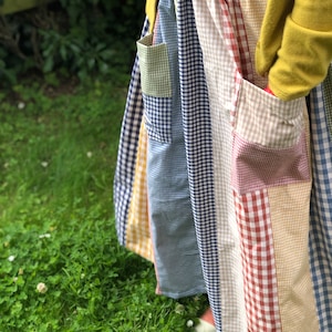 Könnte beinhalten: Ein Patchwork-Rock mit verschiedenen Vichy-Mustern in Blau, Gelb, Rot und Beige. Der Rock hat Taschen und wird mit einem marineblauen Oberteil und einer gelben Strickjacke getragen. Der Rock ist knielang und scheint handgefertigt zu sein.