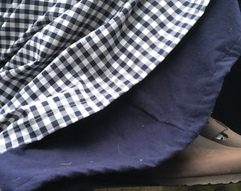 May include: A navy blue and white gingham fabric draped over a solid navy blue fabric. The edge of a brown leather shoe is visible in the lower right corner. The fabrics are layered, creating a textured effect.