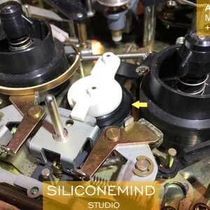 May include: Close-up of the inner workings of an Akai MG1212 cassette deck. The image shows a black plastic reel with a spring, a white plastic gear, and a gold metal lever.