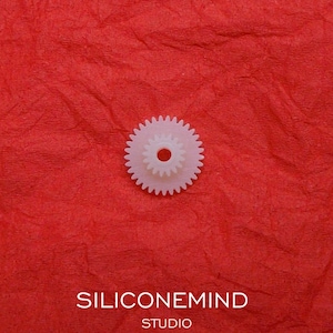 Puede incluir: Engranaje de plástico blanco con un agujero central. El engranaje está sobre una superficie roja texturizada. SONY D82 D88 D90 D99 D150 D250 SILICONEMIND STUDIO