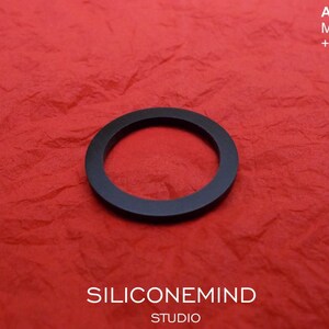 May include: A black rubber ring on a red textured surface. The text "AKAI MG1212 +[?...]", "SILICONEMIND STUDIO" is visible on the surface.
