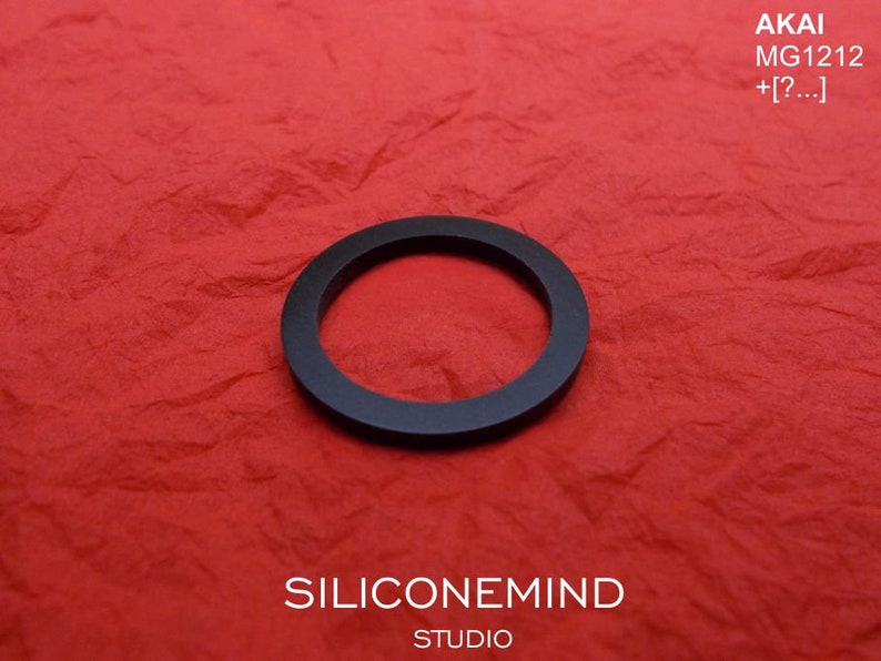 May include: A black rubber ring on a red textured surface. The text "AKAI MG1212 +[?...]", "SILICONEMIND STUDIO" is visible on the surface.