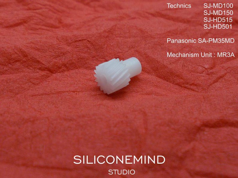 May include: A small, white plastic gear with a cylindrical post, set against a textured red background. The image includes text indicating compatibility with Technics and Panasonic audio equipment models, including SJ-MD100, SJ-MD150, and SA-PM35MD.