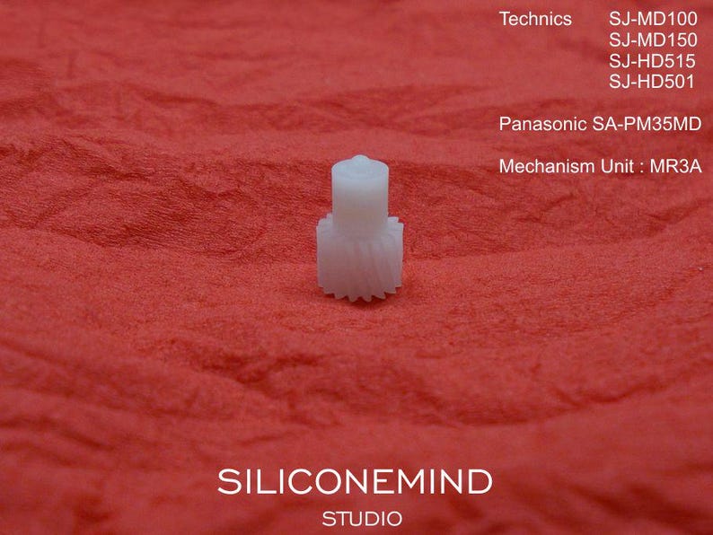 May include: A small, white plastic gear with a cylindrical top and toothed base, set against a textured red background. The image includes text indicating compatibility with Technics and Panasonic models, and the text "SILICONEMIND STUDIO".