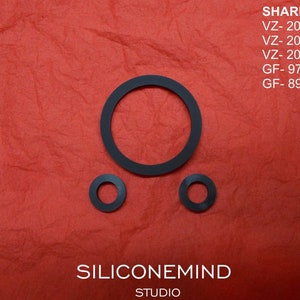 May include: Three black rubber washers of varying sizes are arranged on a textured red background. The image includes the text "SHARP" followed by model numbers and the text "SILICONEMIND STUDIO".