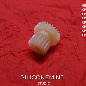 May include: A white plastic gear with a large number of teeth. The gear is on a red background. The text "SILICONEMIND STUDIO" is visible below the gear. The text "ONKYO" and a list of model numbers are visible above the gear.