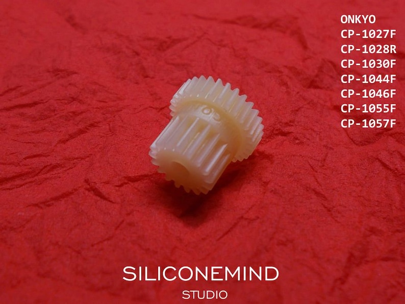 May include: A white plastic gear with a large number of teeth. The gear is on a red background. The text "SILICONEMIND STUDIO" is visible below the gear. The text "ONKYO" and a list of model numbers are visible above the gear.