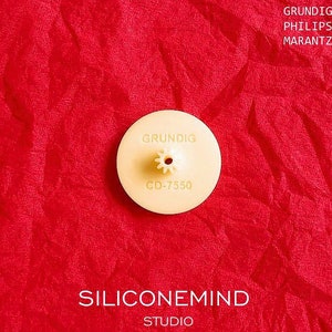May include: A beige plastic CD player gear with the text "GRUNDIG CD-7350" printed on it. The gear is on a red surface.
