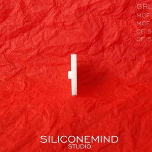 Puede incluir: Una perilla de pl&aacute;stico blanca con forma cuadrada y un peque&ntilde;o agujero en el centro. La perilla est&aacute; sobre un fondo rojo.