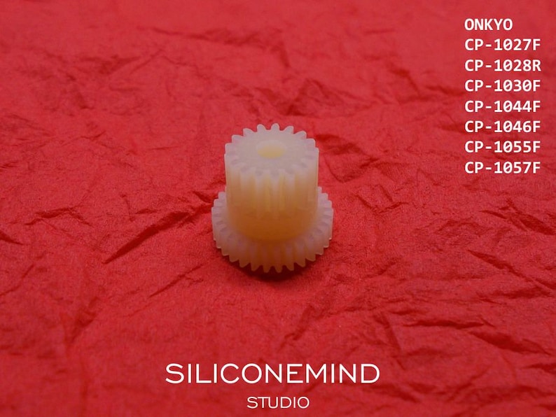 May include: A white plastic gear with a central hole. The gear is on a red background. The text "ONKYO" and a list of model numbers are visible in the background.