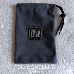 Könnte beinhalten: Ein dunkelgrauer Beutel mit Kordelzug und schwarzem Kordelverschluss. Der Beutel hat einen rechteckigen Aufnäher mit den weißen Worten "Mini Disc". Der Text "SILICONEMIND STUDIO" ist unten aufgedruckt.