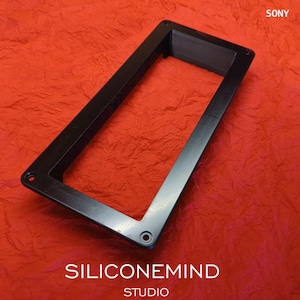 K&ouml;nnte beinhalten: Ein schwarzer rechteckiger Rahmen mit einer hohlen Mitte und vier Schraubl&ouml;chern an den Ecken, konzipiert f&uuml;r die Modelle Sony TC-630 und TC-630D. Der Rahmen hat eine glatte, flache Oberfl&auml;che und ist schr&auml;g positioniert, mit dem Text SONY TC-630 TC-630D in der oberen rechten Ecke und SILICONEMIND STUDIO am unteren Rand.