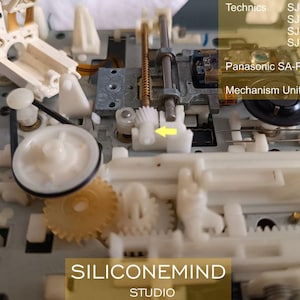 May include: Detailed view of a dismantled electronic mechanism featuring white and beige plastic parts, gears, and metal rods. Text includes "Technics," model numbers, "Panasonic SA-PM35MD," and "Mechanism Unit: MR3A." The logo "SILICONEMIND STUDIO" is also visible.
