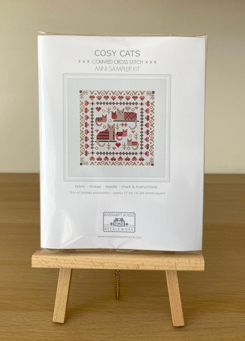 May include: A cross stitch kit titled "Cosy Cats" with a mini sampler kit. The kit includes fabric, thread, a needle, a chart, and instructions. The finished embroidery will be approximately 6 3/4 inches square.