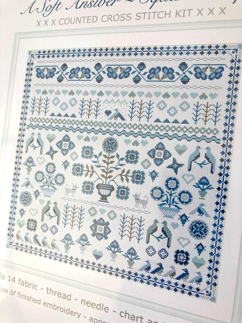 May include: A counted cross stitch kit with a detailed design in shades of blue and white. The design includes floral, bird, and geometric patterns, with the text "A Soft Answer" at the top. The kit includes fabric, thread, and a needle.