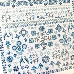 May include: A detailed cross-stitch pattern in shades of blue and white. The design features floral motifs, birds, hearts, and geometric borders. The pattern is on a white background, creating a classic, folk art aesthetic.