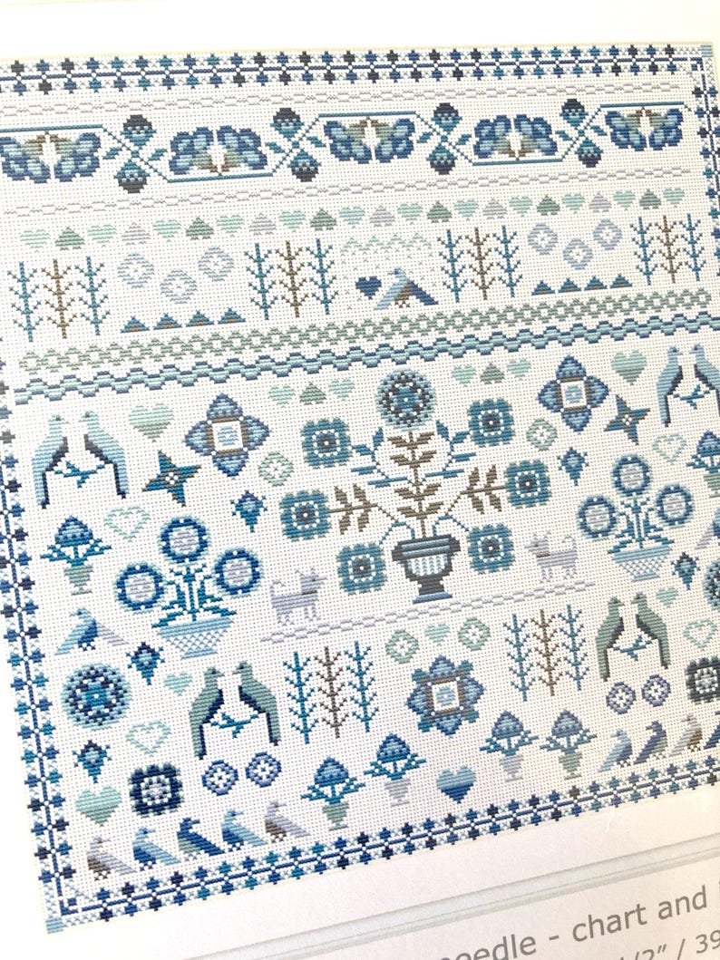 May include: A detailed cross-stitch pattern in shades of blue and white. The design features floral motifs, birds, hearts, and geometric borders. The pattern is on a white background, creating a classic, folk art aesthetic.