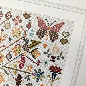 Pu&ograve; includere: Schema di punto croce con un motivo floreale colorato con una farfalla, cuori e forme geometriche. Lo schema &egrave; su tela Aida bianca e include una variet&agrave; di colori, tra cui rosso, arancione, giallo, verde, blu e marrone.