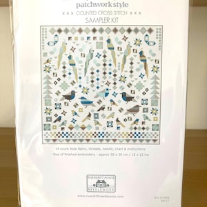 May include: A cross stitch sampler kit featuring a patchwork design of birds. The kit includes 14 count Aida fabric, threads, a needle, a chart, and instructions. The finished embroidery will be approximately 12 inches by 12 inches.