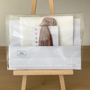 May include: A cross stitch kit with white Aida fabric, floss, and a needle. The kit is packaged in a clear plastic bag and is displayed on a wooden easel. The kit includes the text "Riverdrift House Needlework" and "RHF-14-MSCC RR422".