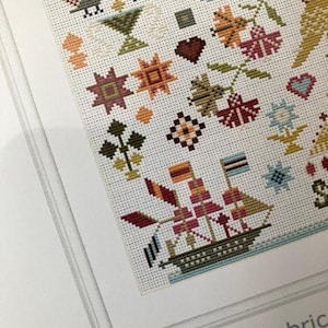 Pu&ograve; includere: Un motivo a punto croce colorato con una variet&agrave; di forme geometriche, fiori e una nave. Il motivo &egrave; su tessuto bianco e include il testo "14 count fabric".