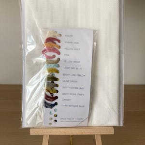 Pu&ograve; includere: Un kit di ricamo a punto croce su tela Aida bianca con una tabella dei colori e gomitoli di filo in crema, rosso ciliegia, oro giallo, rosa, beige giallo, azzurro chiaro, giallo limone chiaro, verde oliva, grigio verde spolverato, verde oliva chiaro, granato e blu antico scuro. Il kit &egrave; etichettato "RR626 Albero di fiori".