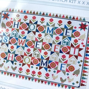 May include: A cross-stitch kit featuring the words "HOME SWEET HOME" in a colorful, geometric design. The design includes houses, flowers, stars, and chickens, with a decorative border. The color palette includes red, blue, green, and brown.