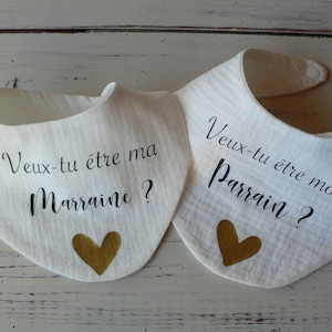 May include: Two white bibs with gold hearts and black text. The text on the left bib reads "Veux-tu &ecirc;tre ma Marraine?" and the text on the right bib reads "Veux-tu &ecirc;tre mon Parrain?"