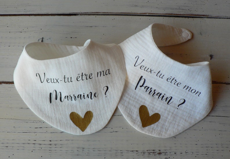 May include: Two white bibs with gold hearts and black text. The text on the left bib reads "Veux-tu &ecirc;tre ma Marraine?" and the text on the right bib reads "Veux-tu &ecirc;tre mon Parrain?"