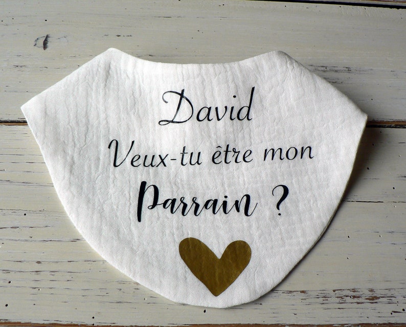 May include: White fabric bib with black text that reads "David Veux-tu &ecirc;tre mon Parrain?" with a gold heart.