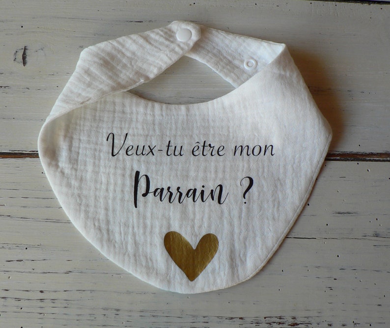 May include: White cotton baby bib with black text that reads "Veux-tu &ecirc;tre mon Parrain?" and a gold heart.