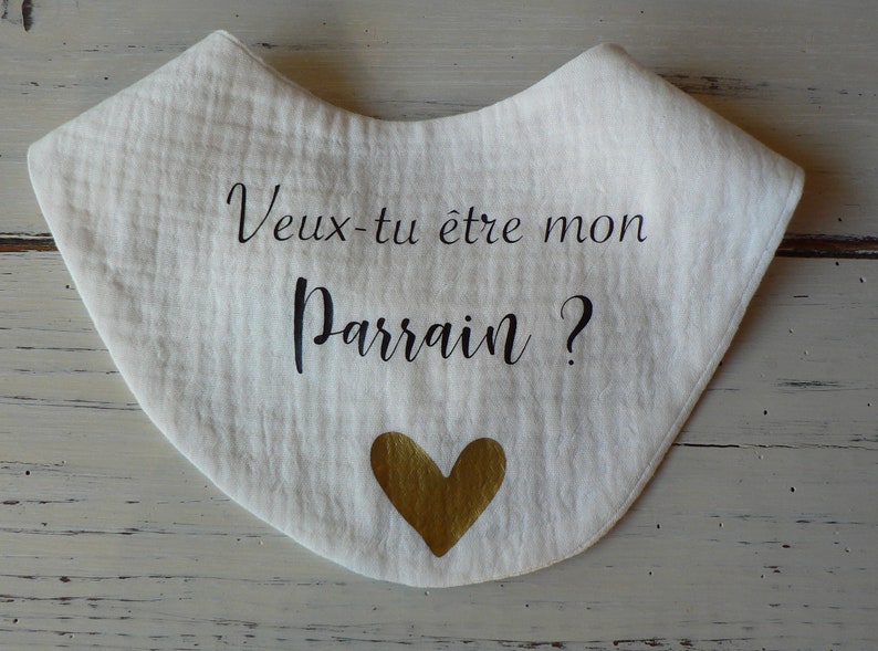 May include: White muslin bib with black text that reads "Veux-tu &ecirc;tre mon Parrain?" and a gold heart.