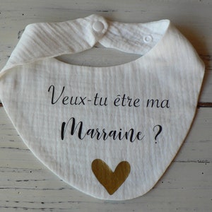May include: White baby bib with the text "Veux-tu &ecirc;tre ma Marraine?" in black lettering and a gold heart.