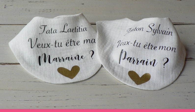 May include: Two white bibs with gold hearts and black text. The text on the left bib reads "Tata Laetitia Veux-tu &ecirc;tre ma Marraine?" and the text on the right bib reads "Anton Sylvain Jeux-tu &ecirc;tre mon Parrain?"