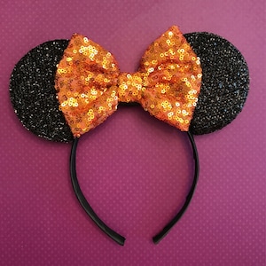 May include: Black and orange sequined Minnie Mouse ears headband with a large bow.