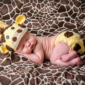 May include: A newborn baby wearing a yellow and brown crocheted giraffe hat and matching diaper cover, sleeping on a brown and white giraffe print blanket.
