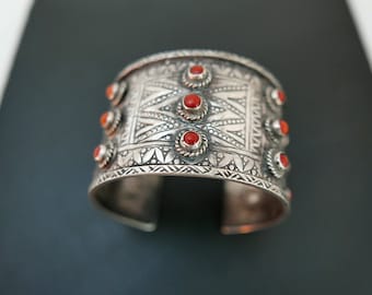 May include: A silver cuff bracelet with intricate geometric designs and red coral stones.