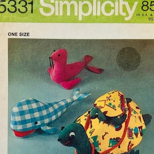 May include: Simplicity sewing pattern 5331 for stuffed animals, featuring a pink seal, a blue and white checkered whale, and a green turtle with a yellow patterned shell. The package includes illustrations of the finished toys and a child.