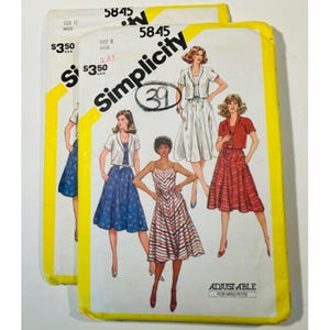 May include: Two vintage Simplicity sewing pattern envelopes. The envelopes are white with yellow accents and feature illustrations of dresses and jackets. The text "Simplicity" and the pattern number "5845" are visible.