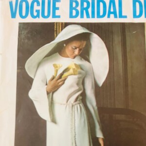 May include: A vintage sewing pattern envelope titled VOGUE BRIDAL D featuring a white long-sleeved gown with a matching wide-brimmed headpiece. The garment includes a braided waist tie and is shown with yellow calla lilies held at the chest.